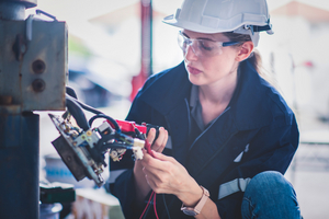 Elektronikerin prüft Industriemaschine mit Messgerät.