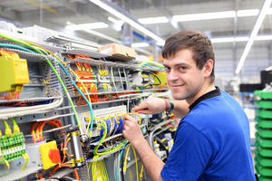 Junger Elektroniker montiert an Schaltwand in einem Werk.