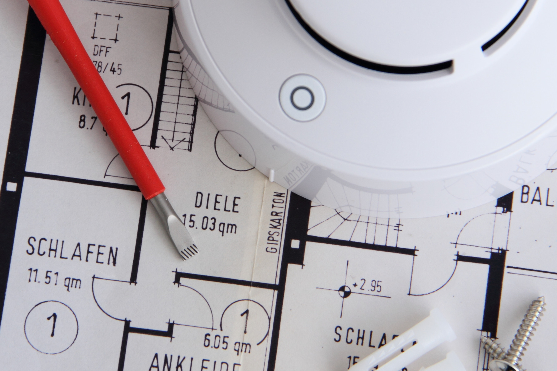 Detailaufnahme: Bauplan, auf dem ein Rauchmelder liegt.