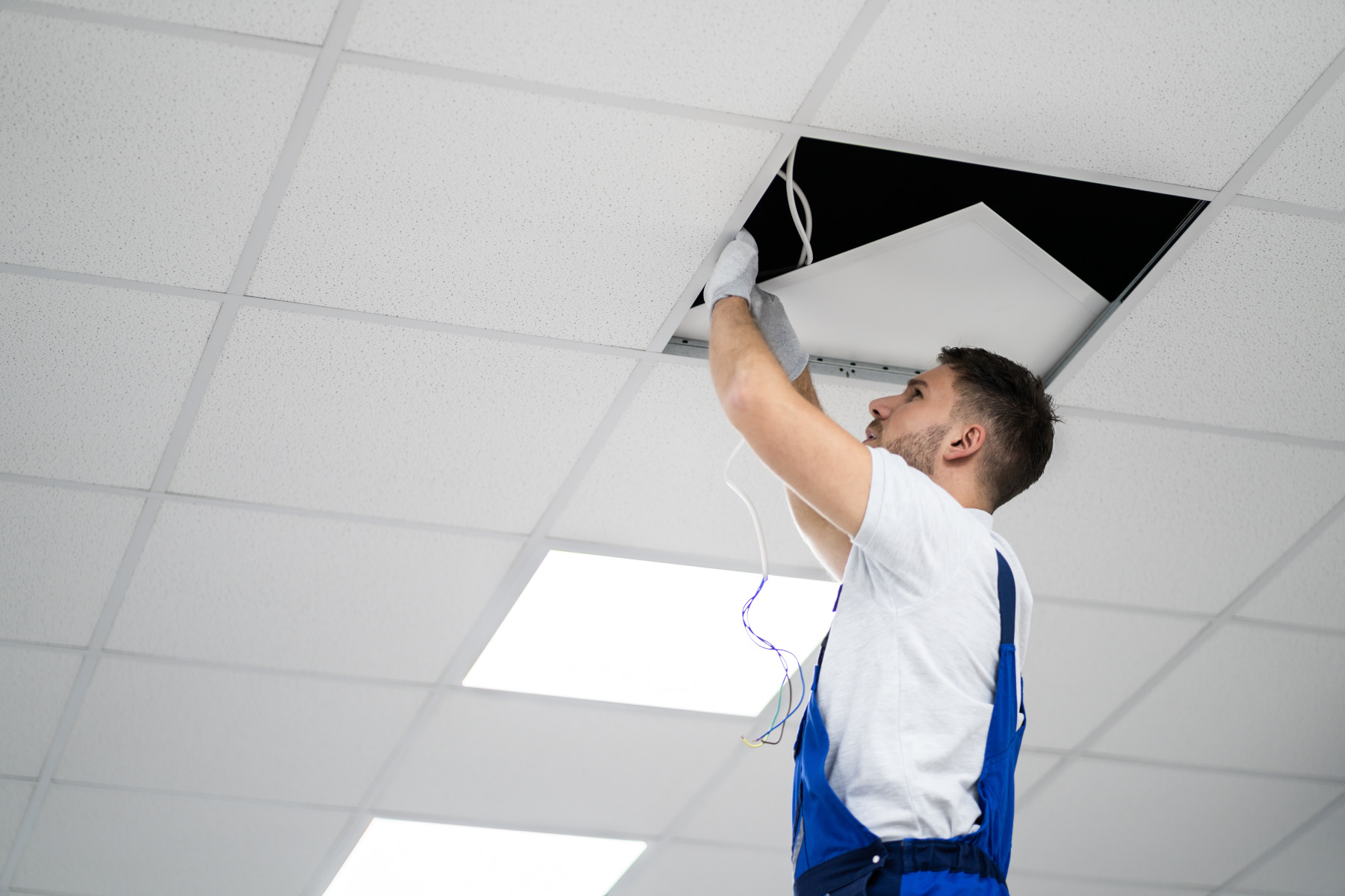 Ein Handwerker installiert Beleuchtung an der Zwischendecke.