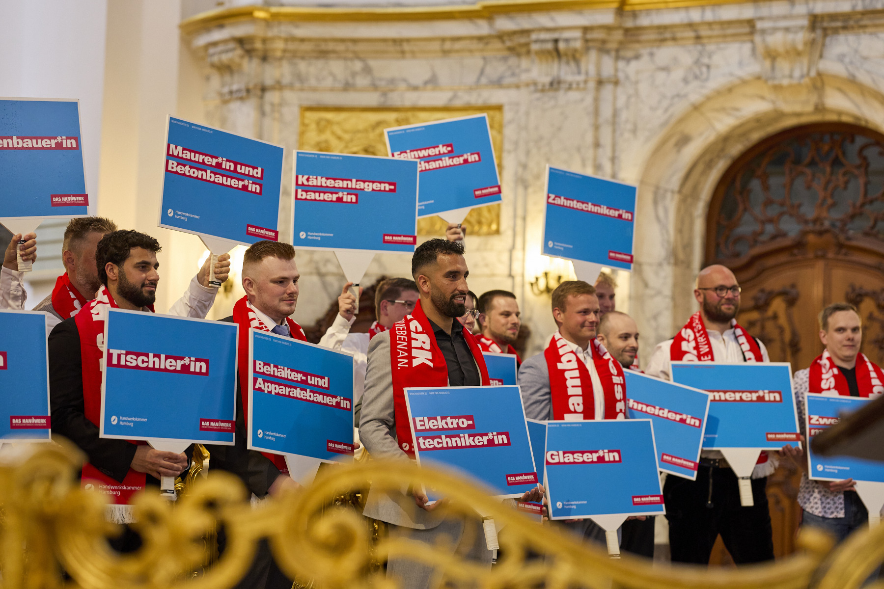 Gruppenbild einiger Jungmeister im Hamburger Michel, die Schilder mit ihrem Beruf halten