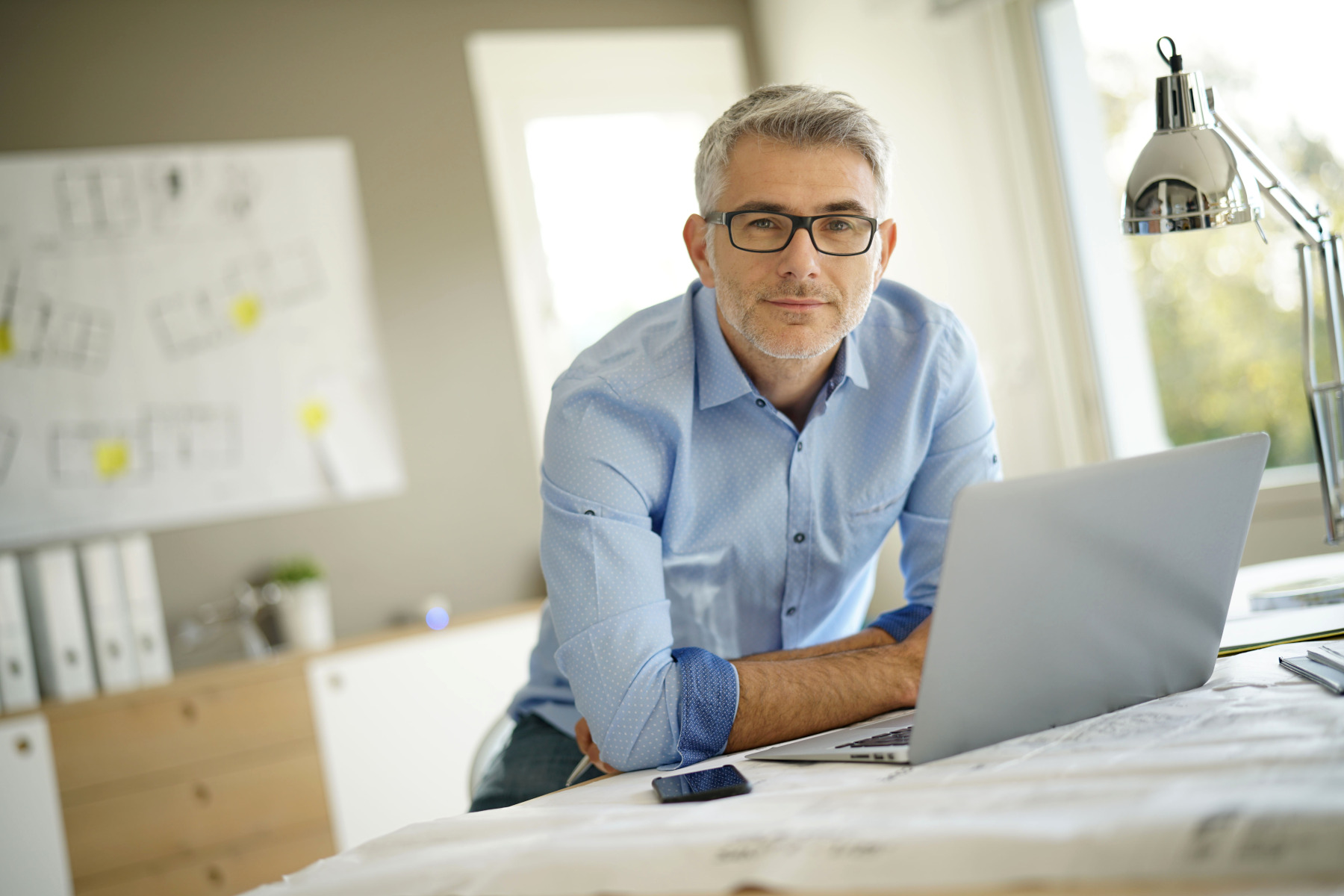 Geschäftsmann arbeitet an Schreibtisch mit Laptop und Bauplänen.